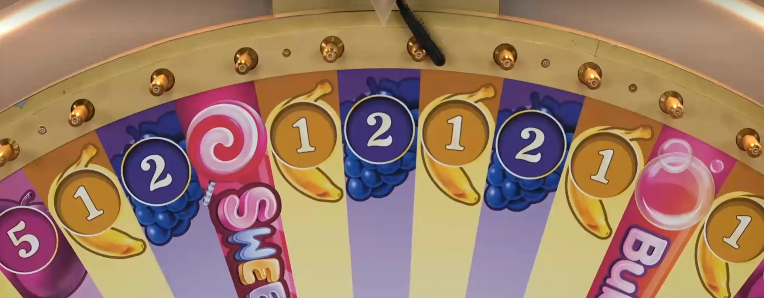 The outer edge of the delightful Sweet Bonanza Candyland features a standing golden wheel adorned with 54 segments, each showcasing a diverse array of sweet treat symbols such as bananas, grapes, and plums.